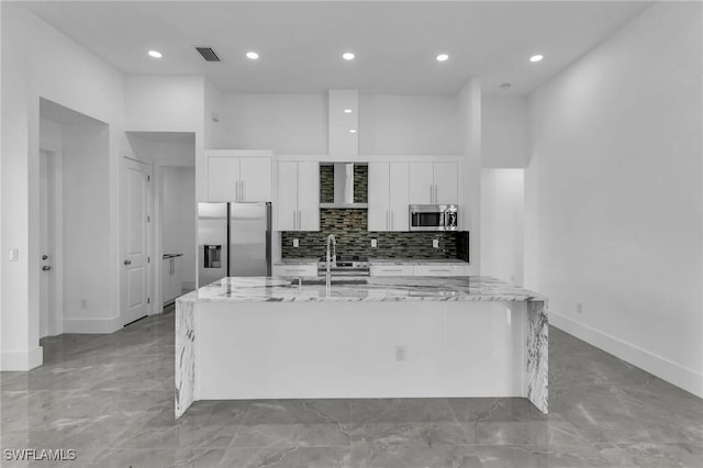 kitchen with white cabinetry, a center island with sink, light stone countertops, and appliances with stainless steel finishes