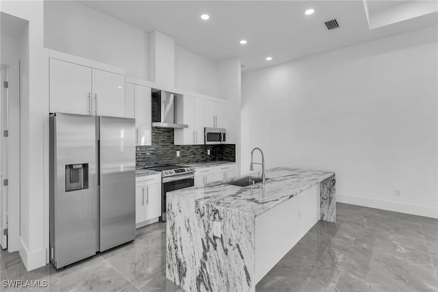 kitchen with light stone countertops, white cabinetry, sink, stainless steel appliances, and wall chimney range hood