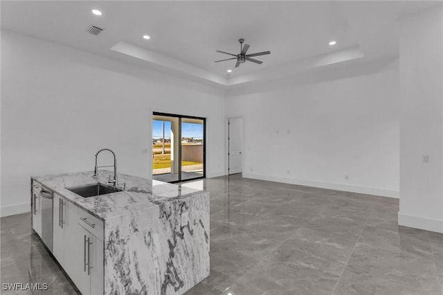 kitchen with a kitchen island with sink, white cabinets, sink, ceiling fan, and a tray ceiling