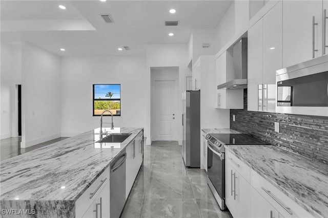 kitchen featuring appliances with stainless steel finishes, backsplash, sink, wall chimney range hood, and white cabinets