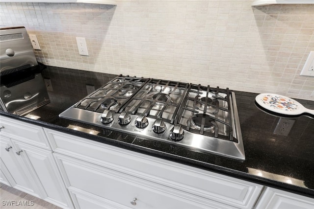room details featuring stainless steel gas stovetop, white cabinets, dark countertops, and backsplash