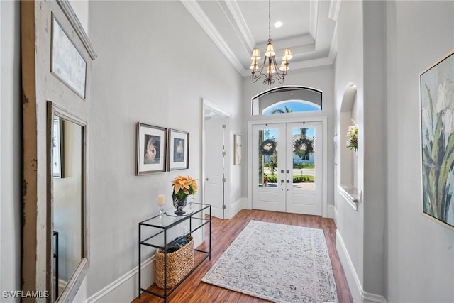 foyer with hardwood / wood-style floors, a raised ceiling, crown molding, a towering ceiling, and a chandelier