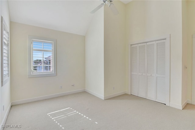 unfurnished bedroom with ceiling fan, a closet, light colored carpet, and vaulted ceiling