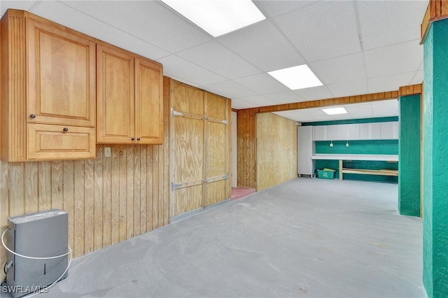 basement featuring wooden walls and a drop ceiling