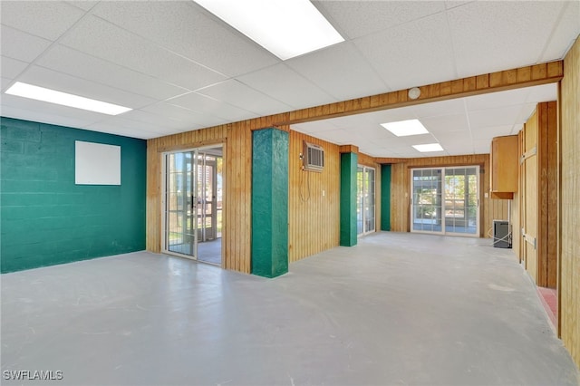 unfurnished living room with a paneled ceiling, wooden walls, and concrete flooring