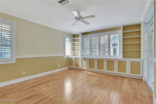 spare room with built in shelves, a wealth of natural light, and light wood-type flooring