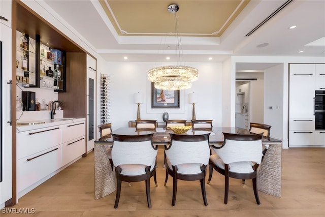 dining room featuring a raised ceiling, sink, ornamental molding, light wood-type flooring, and a chandelier