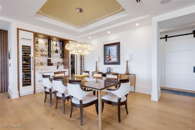 dining area featuring light wood-type flooring, a raised ceiling, sink, a barn door, and a chandelier