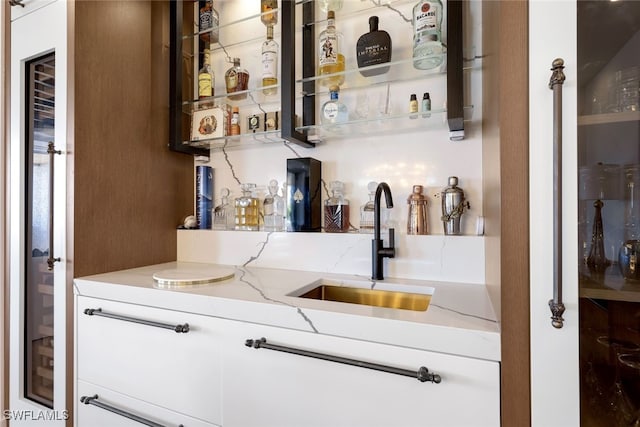 bar featuring white cabinets, light stone countertops, and sink