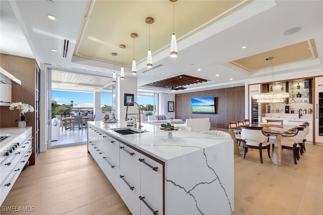 kitchen with a raised ceiling, sink, pendant lighting, white cabinets, and an island with sink