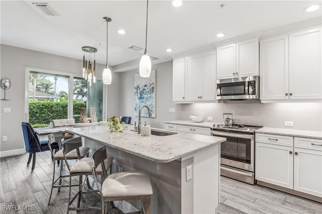 kitchen featuring pendant lighting, a kitchen island with sink, white cabinets, sink, and appliances with stainless steel finishes