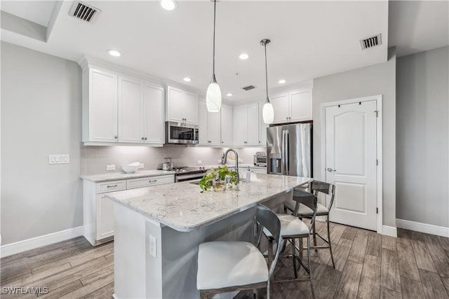 kitchen with white cabinets, a kitchen island with sink, appliances with stainless steel finishes, and light hardwood / wood-style flooring