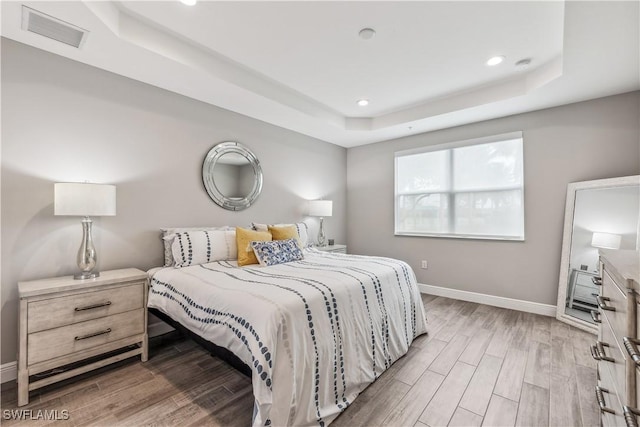 bedroom with light hardwood / wood-style floors and a raised ceiling