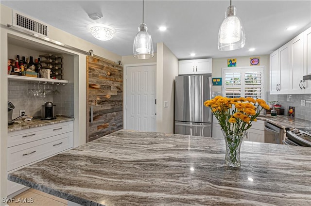 kitchen featuring decorative backsplash, a barn door, appliances with stainless steel finishes, light stone counters, and white cabinetry