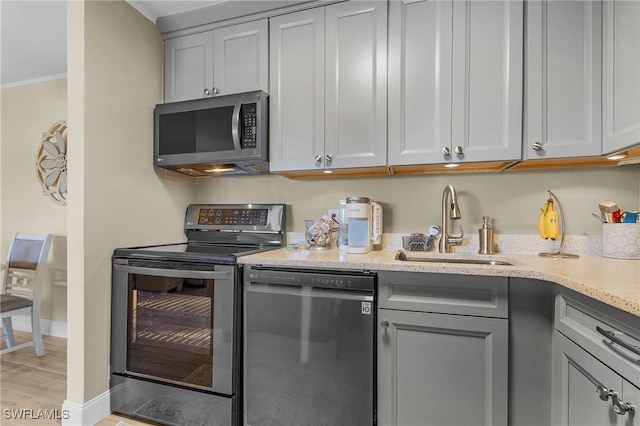 kitchen with gray cabinetry, sink, ornamental molding, light wood-type flooring, and stainless steel appliances