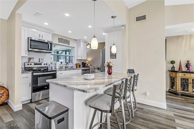 kitchen featuring light stone countertops, hanging light fixtures, dark hardwood / wood-style floors, white cabinets, and appliances with stainless steel finishes