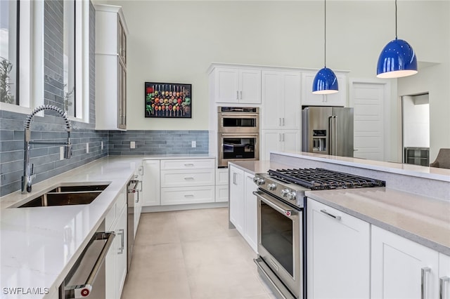 kitchen featuring premium appliances, a sink, white cabinets, hanging light fixtures, and tasteful backsplash