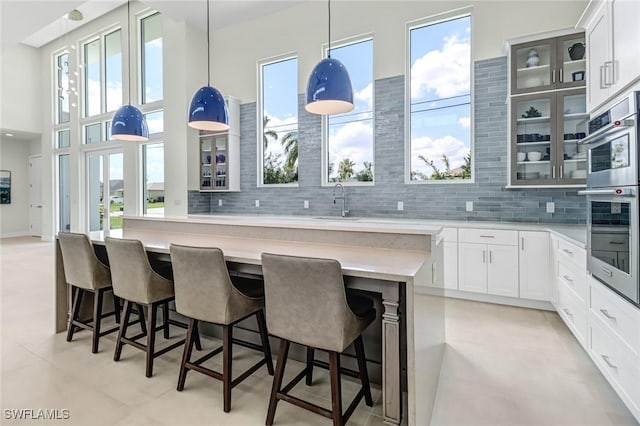 kitchen featuring stainless steel double oven, light countertops, a center island, tasteful backsplash, and glass insert cabinets