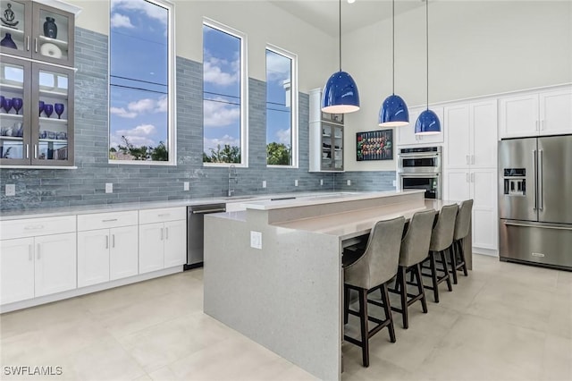 kitchen with a center island, stainless steel appliances, light countertops, decorative backsplash, and glass insert cabinets