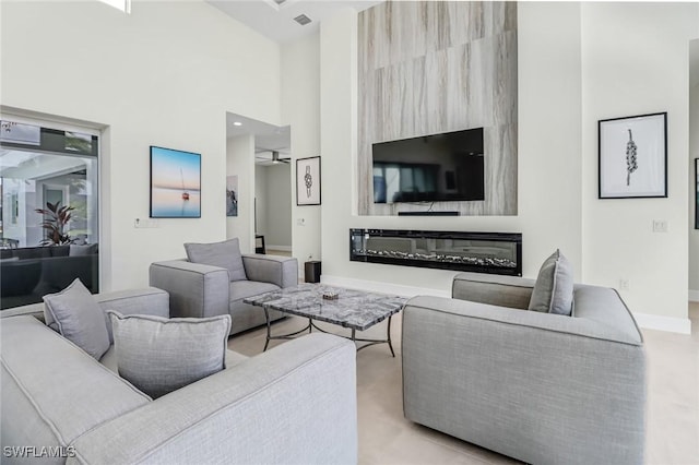 living room with a ceiling fan, a towering ceiling, visible vents, baseboards, and a glass covered fireplace