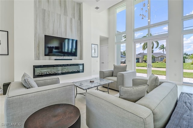 living area with visible vents, a towering ceiling, baseboards, french doors, and a glass covered fireplace