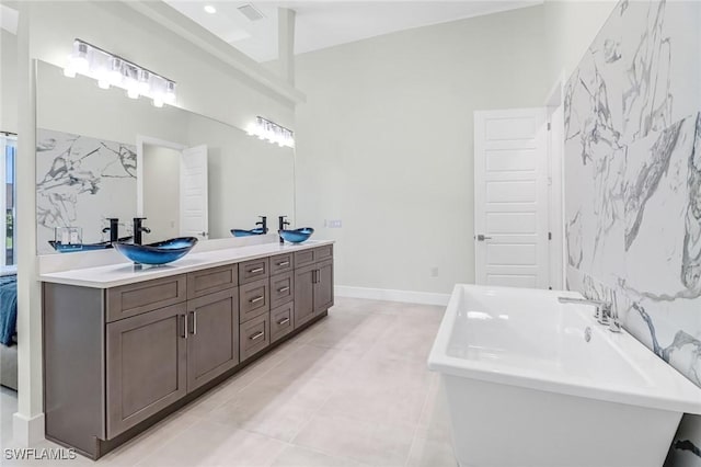 full bath featuring a freestanding tub, a sink, baseboards, tile patterned floors, and double vanity