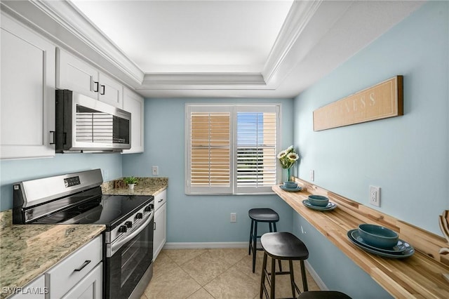 kitchen with a raised ceiling, light stone counters, appliances with stainless steel finishes, a kitchen bar, and white cabinetry