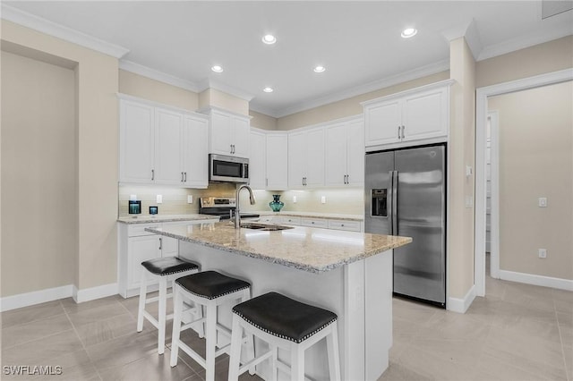 kitchen with light stone countertops, stainless steel appliances, sink, a center island with sink, and white cabinetry