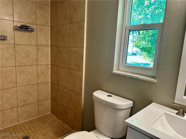 bathroom featuring a tile shower, vanity, and toilet