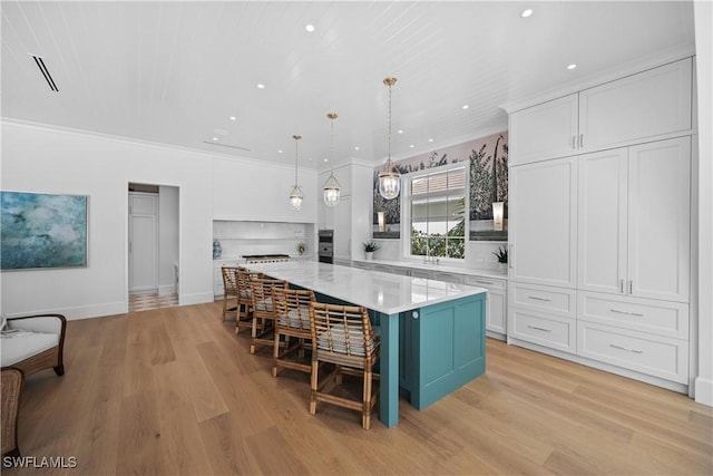 kitchen with a large island, white cabinets, hanging light fixtures, ornamental molding, and light hardwood / wood-style flooring