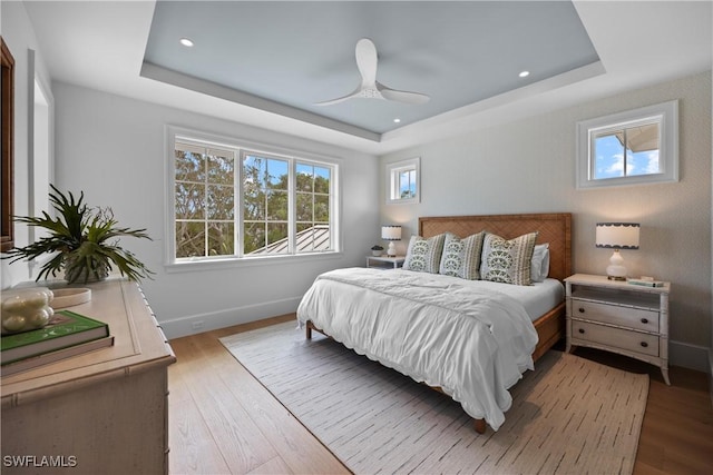 bedroom with ceiling fan, a tray ceiling, and hardwood / wood-style flooring