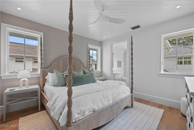 bedroom featuring ceiling fan, multiple windows, ensuite bath, and light wood-type flooring