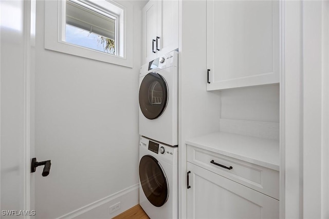 clothes washing area with cabinets and stacked washer / dryer