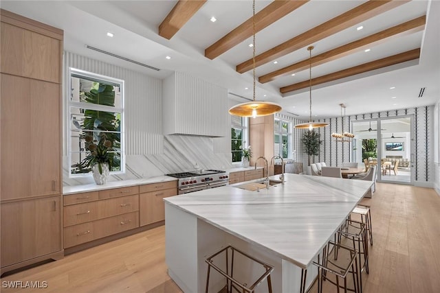 kitchen featuring a large island, sink, backsplash, decorative light fixtures, and high end range