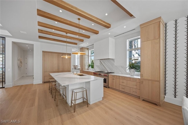 kitchen featuring pendant lighting, stainless steel stove, light hardwood / wood-style flooring, and an island with sink