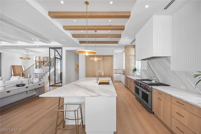 kitchen with double oven range, a spacious island, decorative light fixtures, beam ceiling, and light stone counters