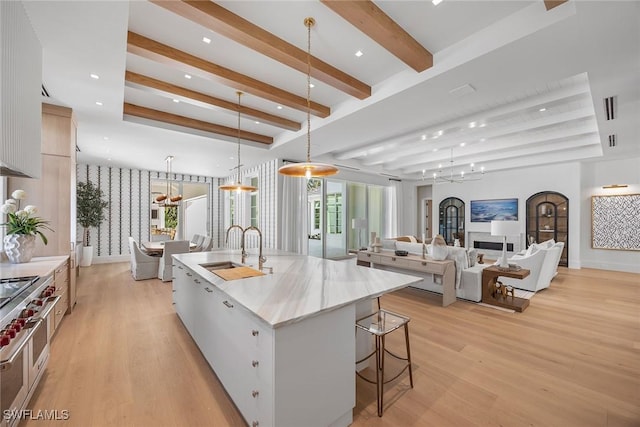 kitchen with a large island, sink, pendant lighting, white cabinets, and light wood-type flooring