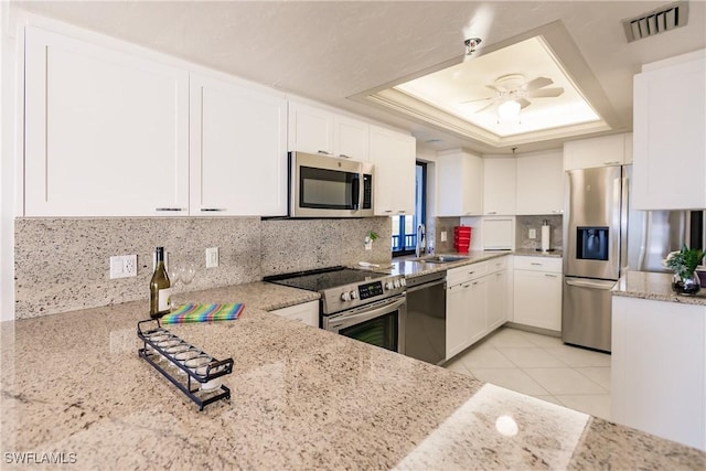 kitchen with appliances with stainless steel finishes, light stone counters, a tray ceiling, sink, and white cabinets