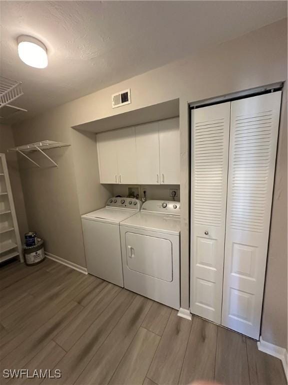 clothes washing area with cabinets, light wood-type flooring, and washing machine and clothes dryer