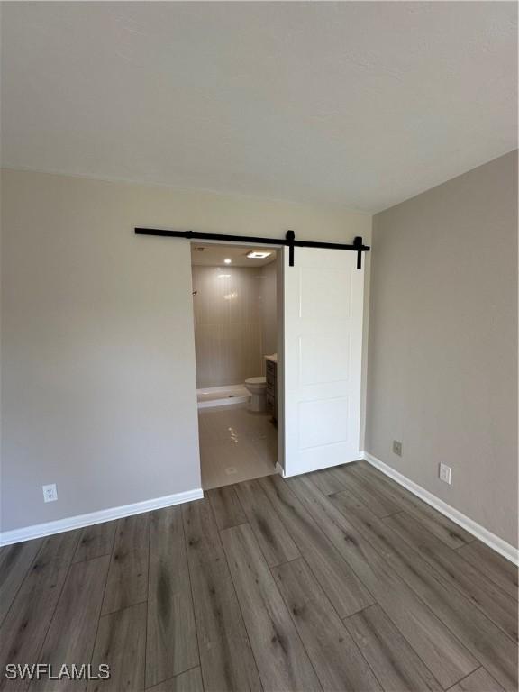 unfurnished bedroom featuring hardwood / wood-style flooring, ensuite bathroom, and a barn door