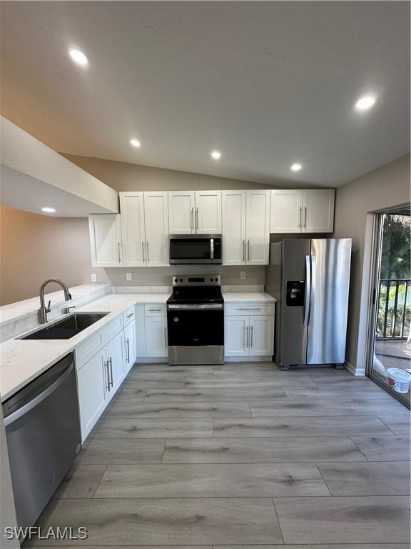 kitchen with white cabinets, sink, lofted ceiling, and stainless steel appliances