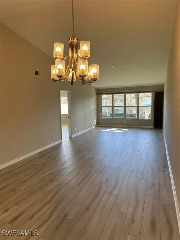 unfurnished room featuring wood-type flooring, an inviting chandelier, and lofted ceiling