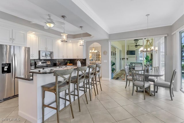 kitchen with white cabinets, ceiling fan with notable chandelier, a kitchen breakfast bar, hanging light fixtures, and appliances with stainless steel finishes