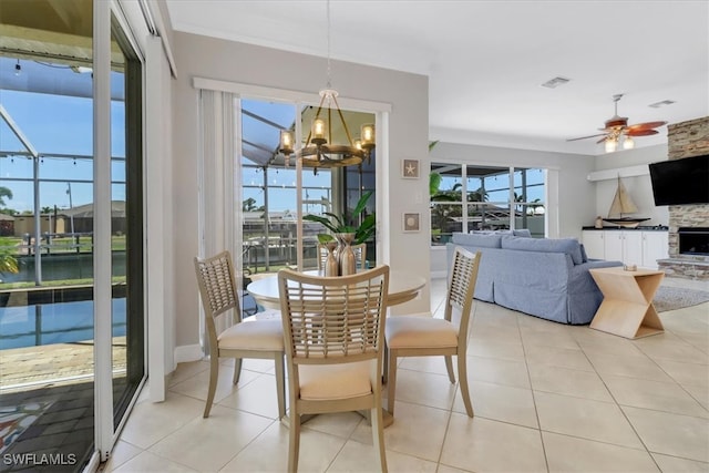 tiled dining space featuring a fireplace, ceiling fan with notable chandelier, and a water view