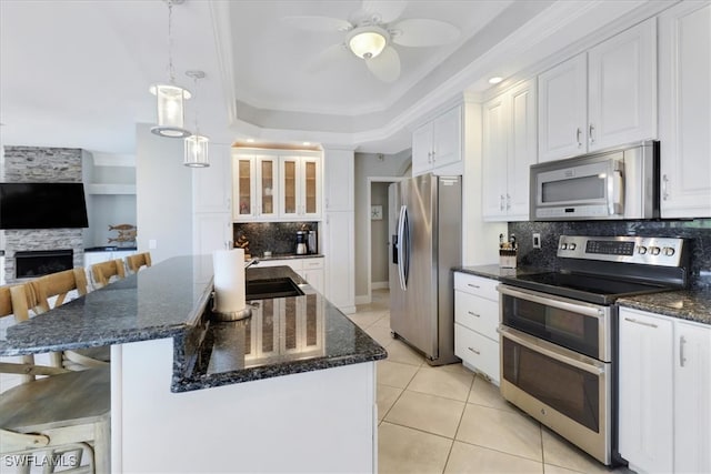 kitchen with a kitchen bar, appliances with stainless steel finishes, pendant lighting, a premium fireplace, and white cabinets