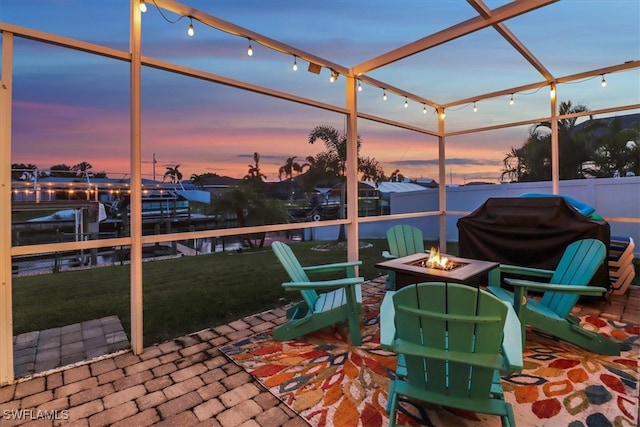 patio terrace at dusk featuring a yard, a water view, a fire pit, and a grill