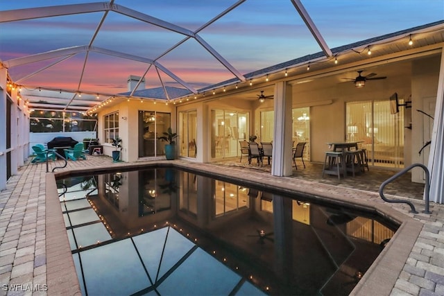 pool at dusk with a patio area, ceiling fan, and glass enclosure