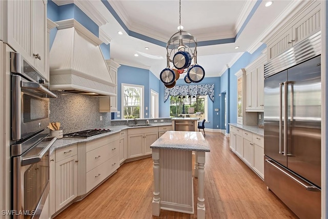 kitchen featuring light stone counters, stainless steel appliances, a tray ceiling, pendant lighting, and a kitchen island