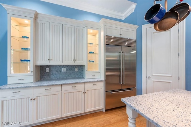 kitchen with built in fridge, white cabinets, decorative backsplash, light stone countertops, and ornamental molding