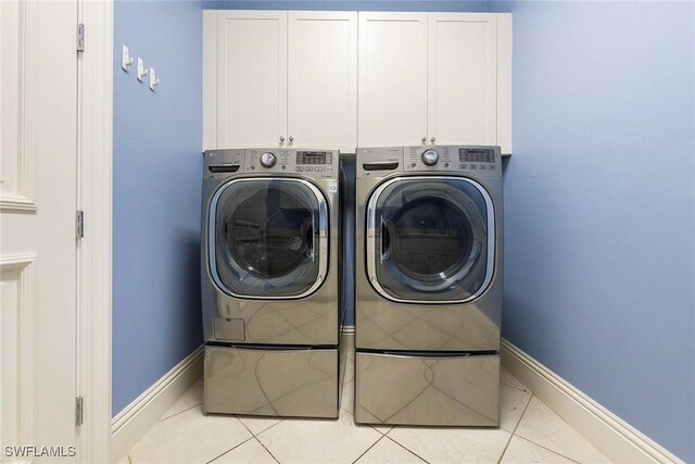 washroom featuring washing machine and dryer, light tile patterned floors, and cabinets